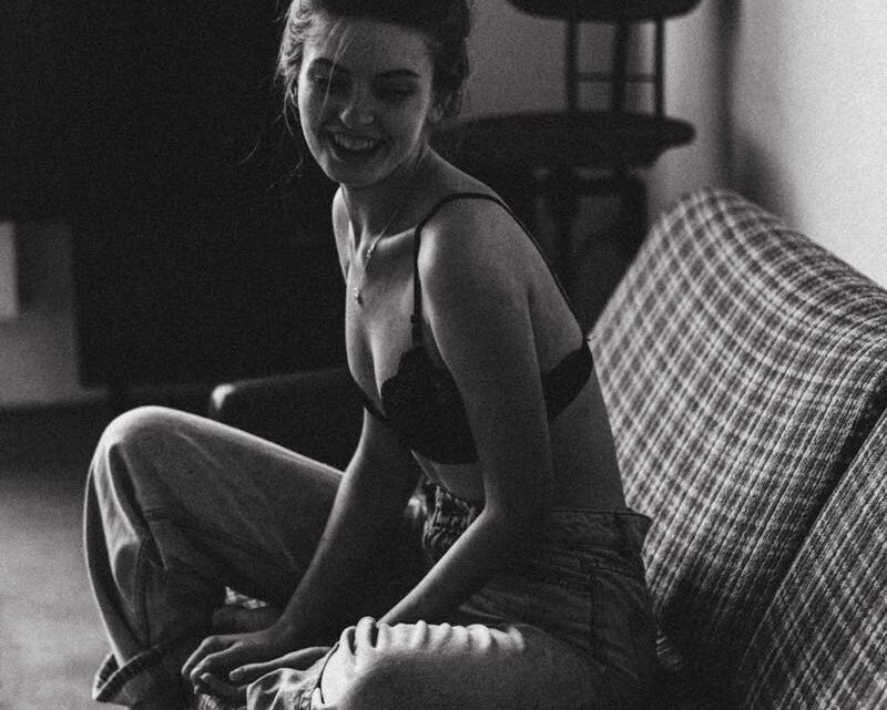 Smiling Young Woman in Bra and Jeans Sitting on the Couch