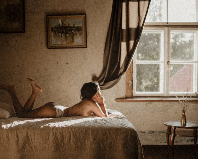 Side view unrecognizable slim female in white panties resting on comfortable bed in light bedroom with old fashioned interior items